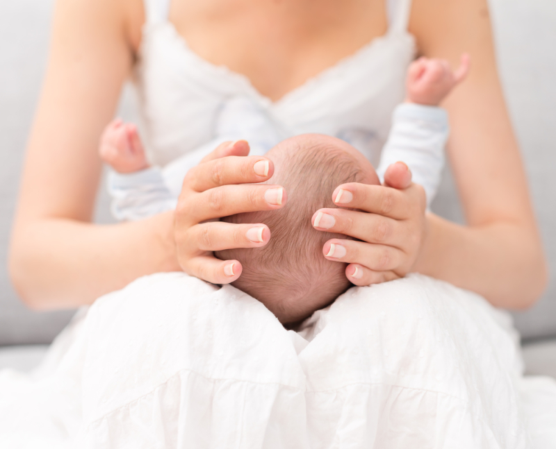 Mother is holding newborn baby on her knees.
