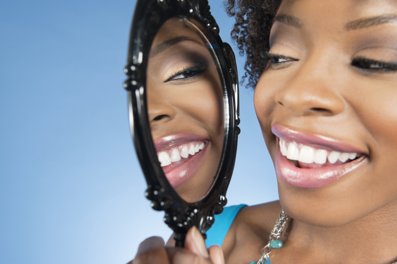 Close-up of a young woman looking at herself in mirror and smiling over colored background