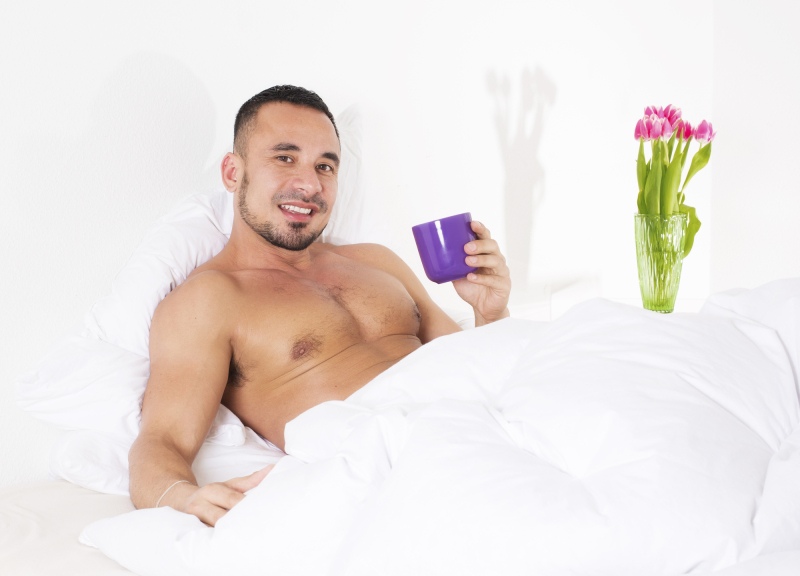 man in bed with naked torso holding a cup