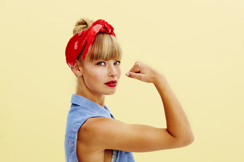 Strong young blond woman flexing muscle, portrait