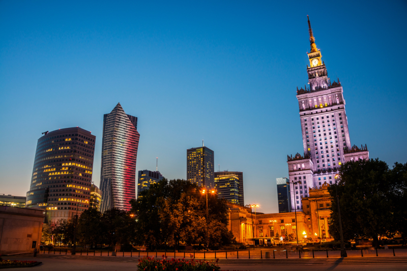 Illuminated Palace of Culture and Science in downtown of Warsaw, Poland. Modern business skyscrapers at night with sunset clear blue sky