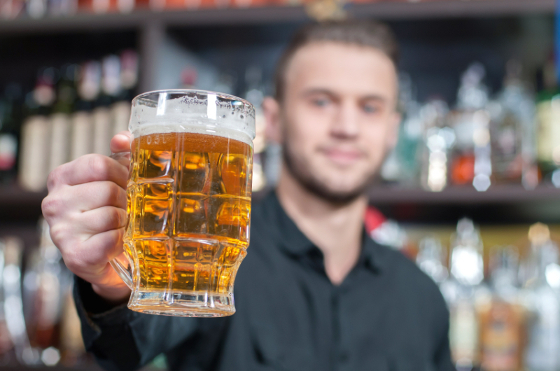 Young smiling bartender with beer on the bar