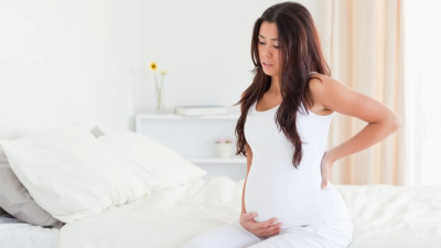 Beautiful pregnant woman holding her back while sitting on a bed