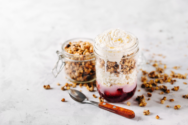 Healthy breakfast with granola, jam and cream in a glass jar