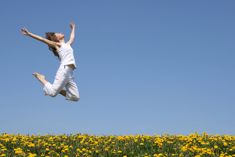 Young woman in a beautiful happy jump in flowering field.