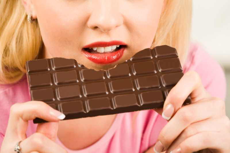 Close-up of female holding a bar of milk chocolate and eating it