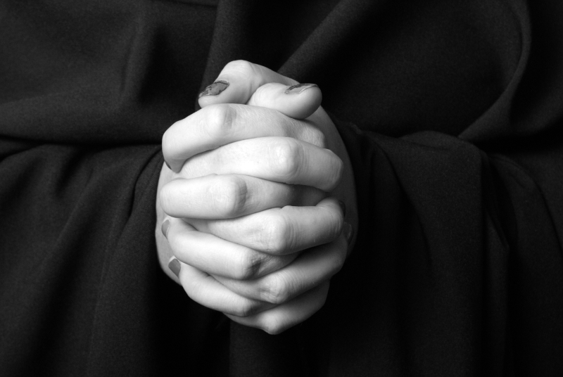 A black and white image of a womans hands clasped in prayer.