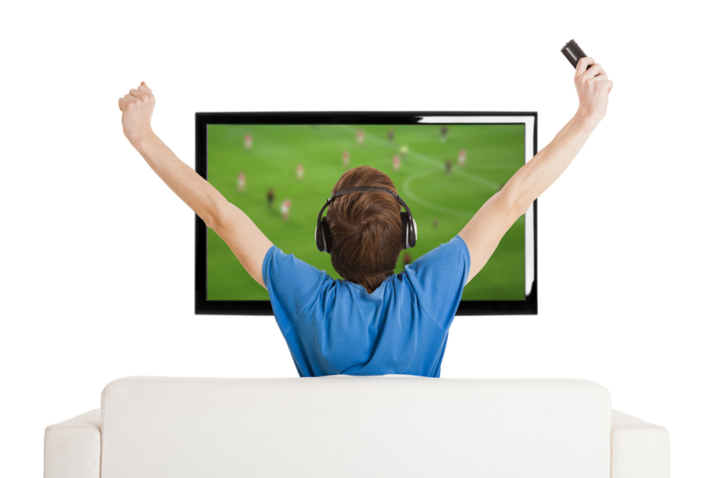 Young man sitting on the couch watching a football game on tv with arms up