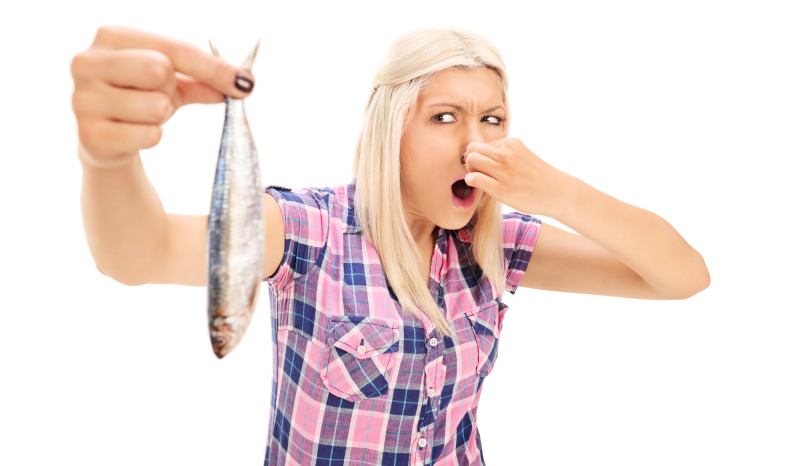 Blond woman holding a stinky fish isolated on white background