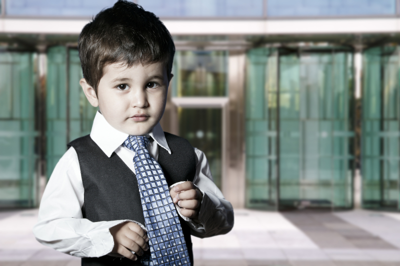 child dressed businessman smiling in front of building
