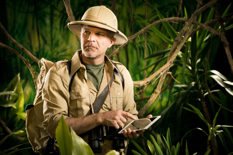 Colonial style adventurer with digital tablet exploring jungle wilderness.