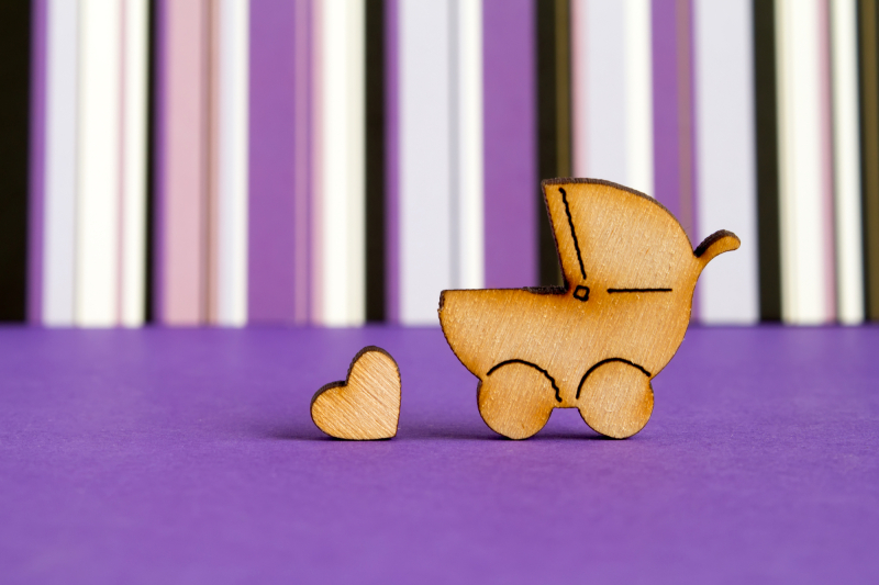 Wooden icon of baby carriage and little heart on purple striped background horizontal