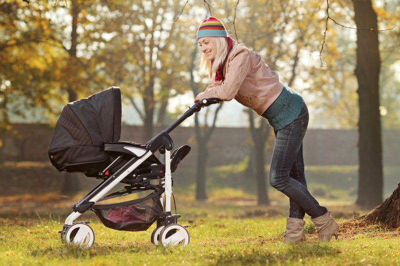 A young mother with a baby carriage walking in a park