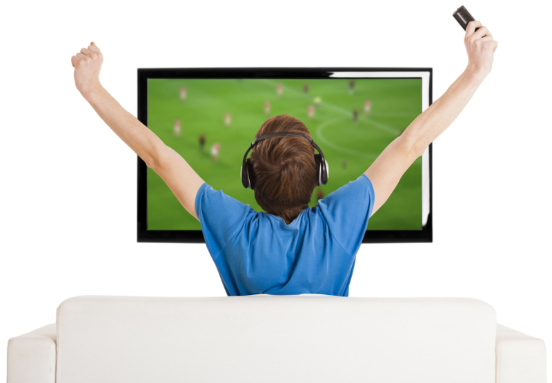 Young man sitting on the couch watching a football game on tv with arms up