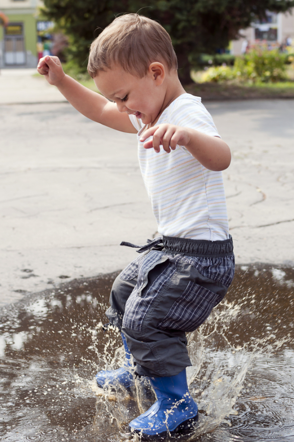Happy child jumping into a street puddle.
