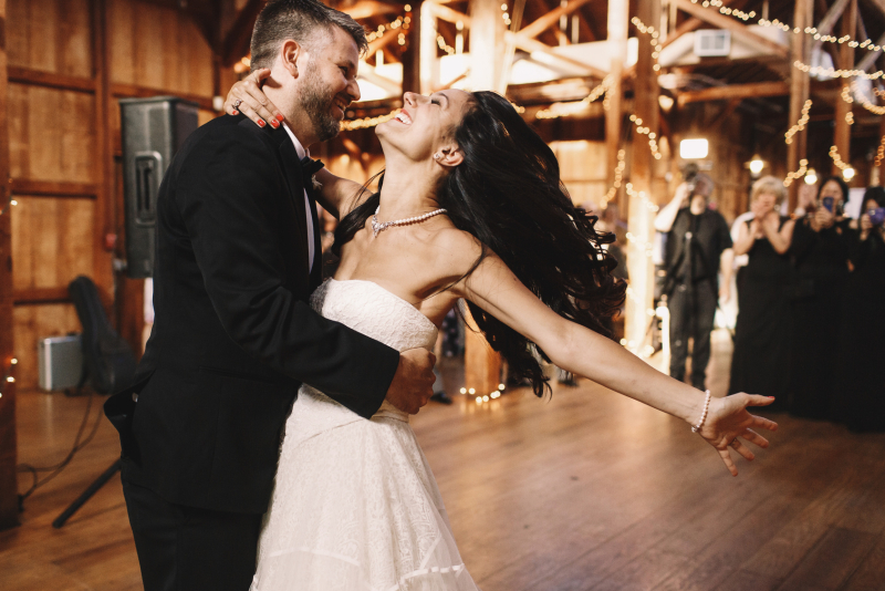 Bride shakes her dark hair while dancing with a groom in wooden hall